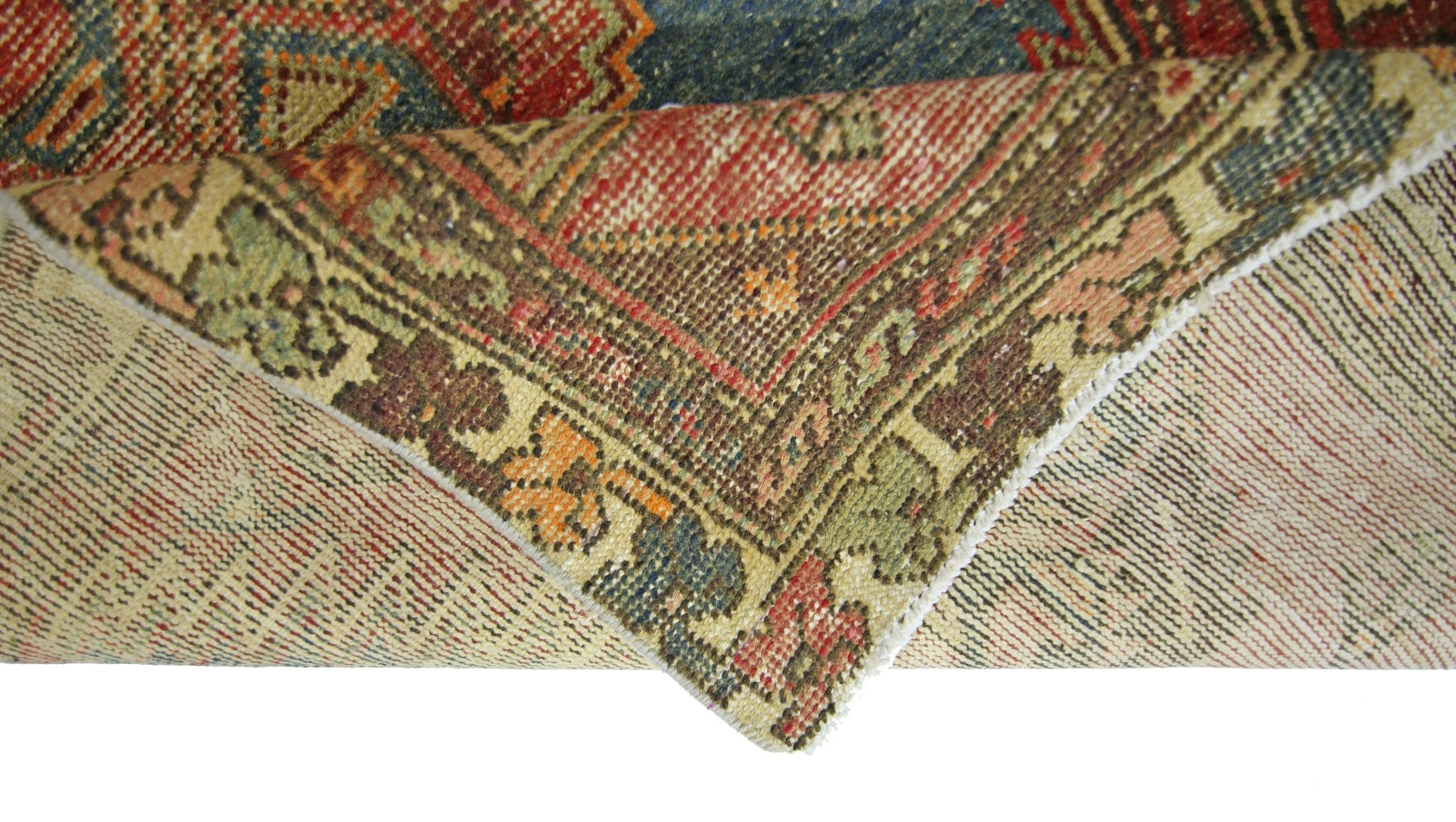 A corner of a vintage Persian Hamadan rug is folded back to reveal its wool pile and cotton base.