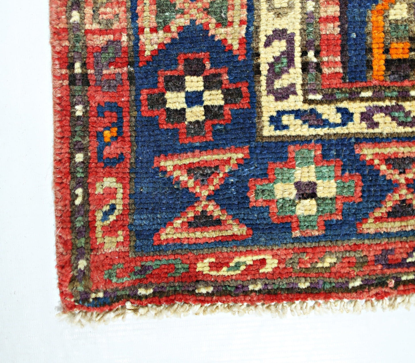 A corner view of a vintage Persian Hamadan rug featuring geometric patterns in red, blue, and green.