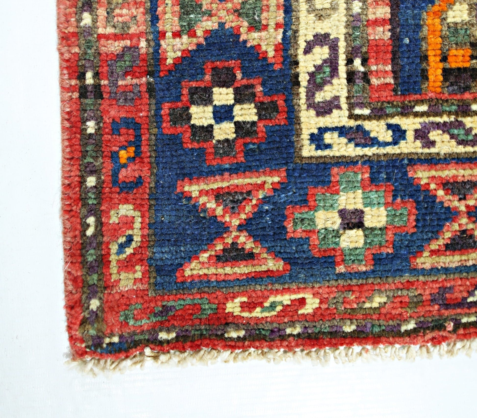 A corner view of a vintage Persian Hamadan rug featuring geometric patterns in red, blue, and green.