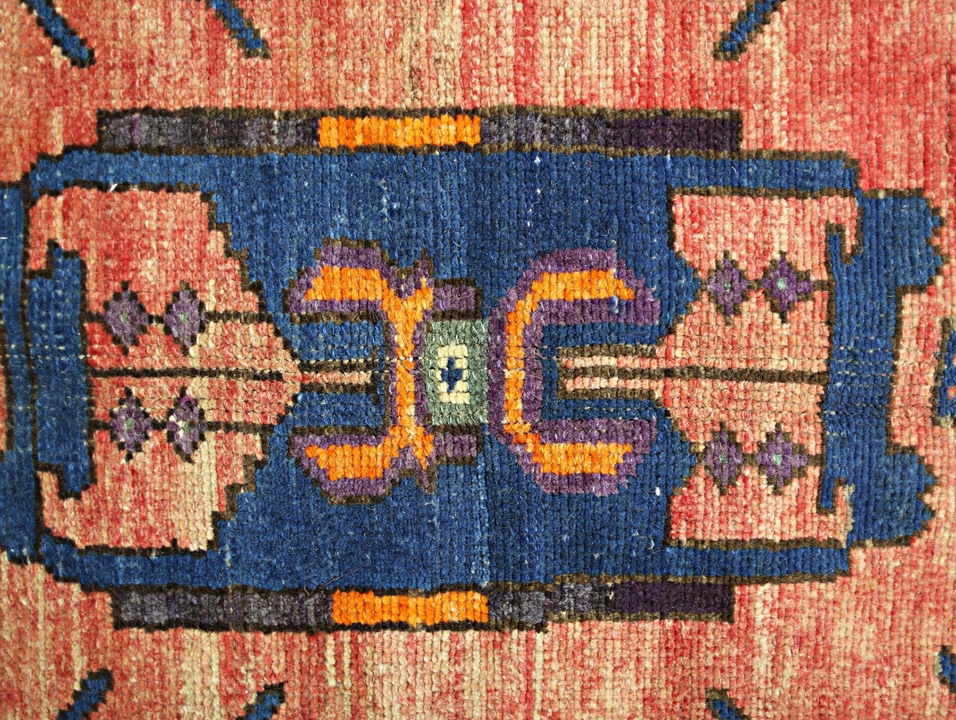 A close-up of a vintage Persian Hamadan rug featuring a geometric blue medallion on a red field.