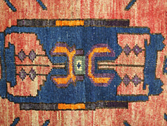 A close-up of a vintage Persian Hamadan rug featuring a geometric blue medallion on a red field.
