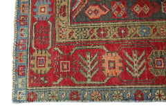 A close-up of a vintage Persian Hamadan rug featuring geometric floral patterns in red, blue, and tan.