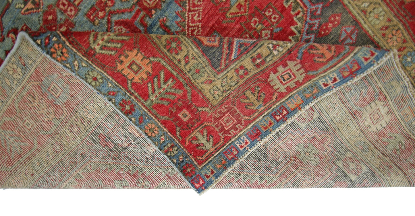 A vintage Persian Hamadan rug with a red and blue geometric pattern folded to show the underside.