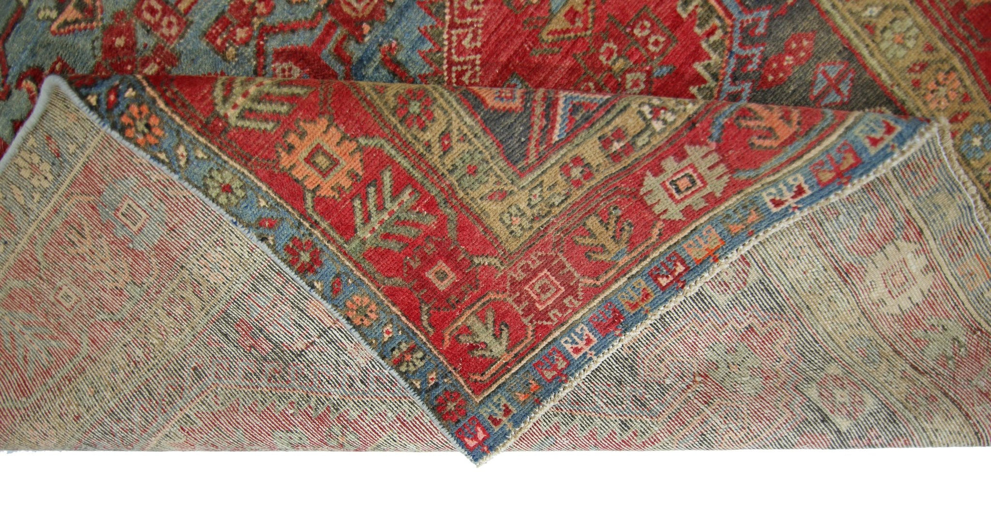 A vintage Persian Hamadan rug with a red and blue geometric pattern folded to show the underside.