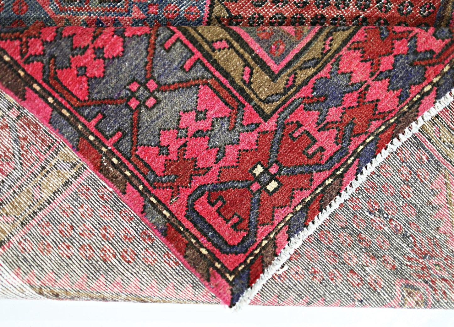 A corner of a vintage Persian Hamadan rug folded over to show its intricate red and blue pattern.