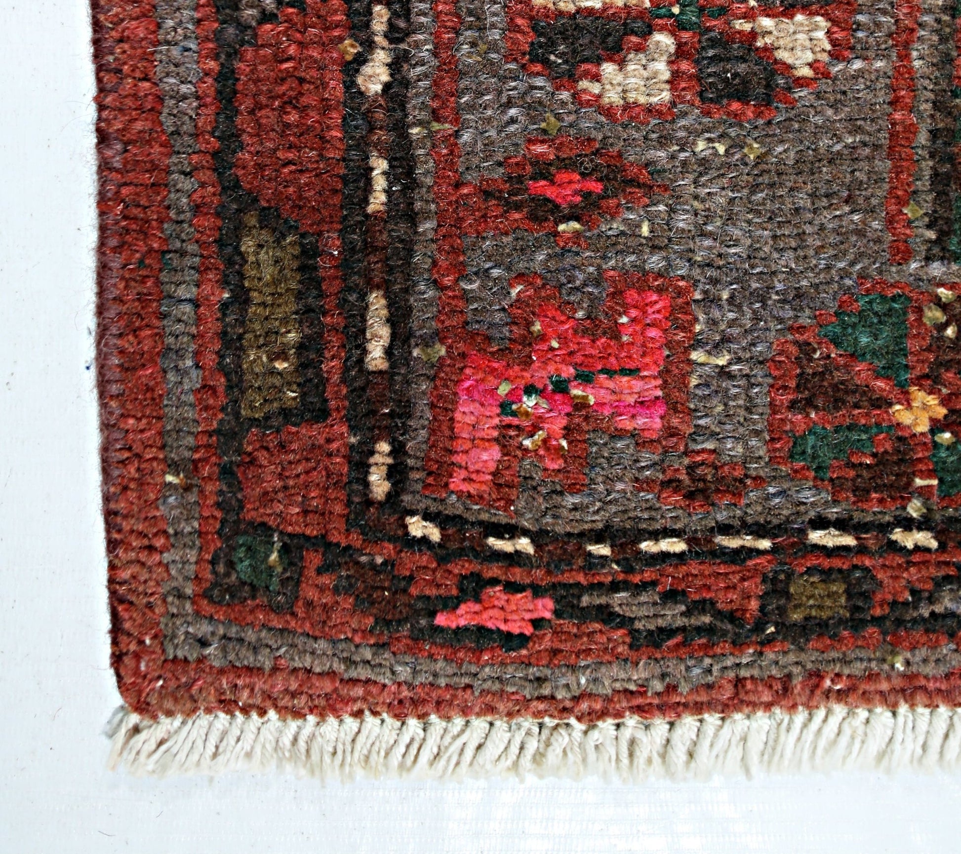A close-up of a vintage Persian Hamadan rug featuring a geometric pattern in red, brown, and green.