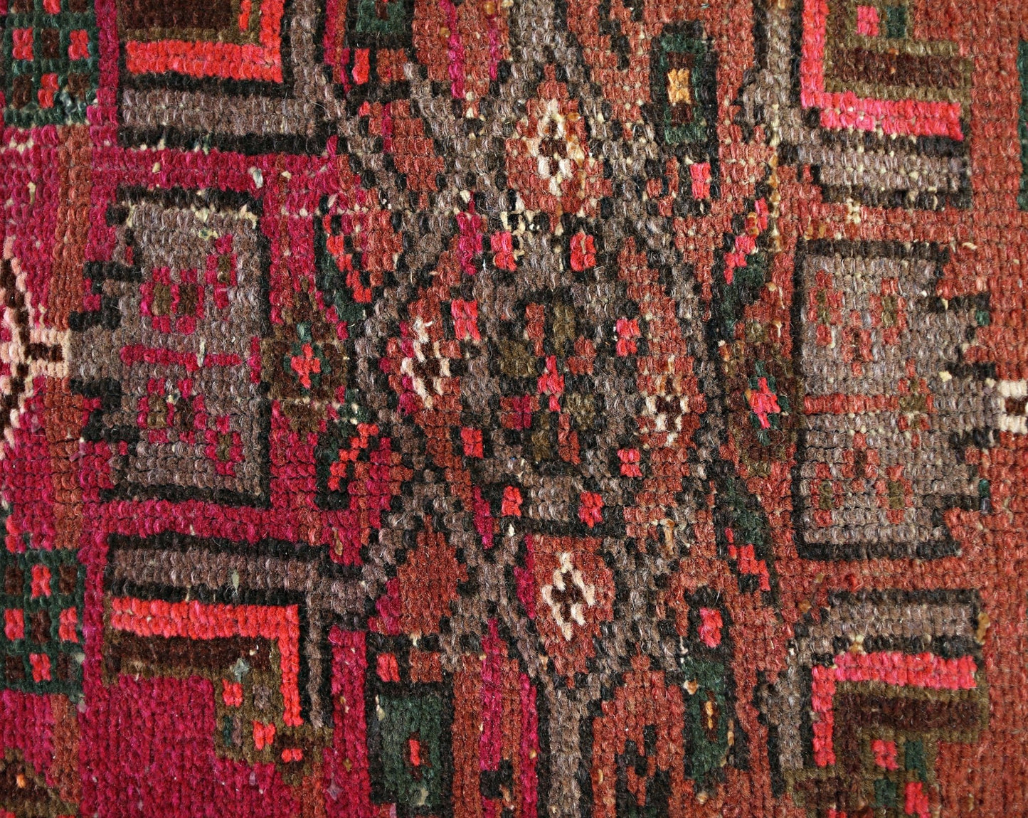 A close-up of a vintage Persian Hamadan rug featuring intricate geometric patterns in red and brown.