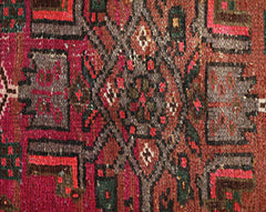 A close-up of a vintage Persian Hamadan rug featuring intricate geometric patterns in red and brown.