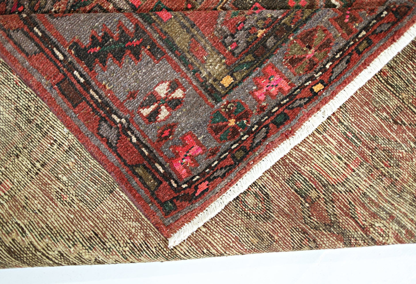 A corner of a vintage Persian Hamadan rug showing a folded edge with intricate geometric patterns.
