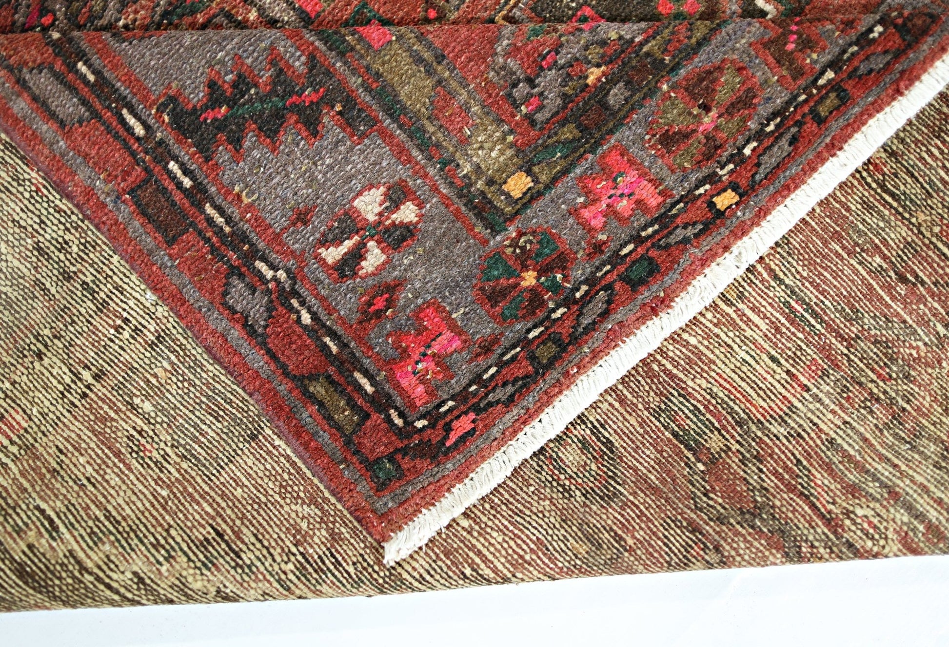 A corner of a vintage Persian Hamadan rug showing a folded edge with intricate geometric patterns.