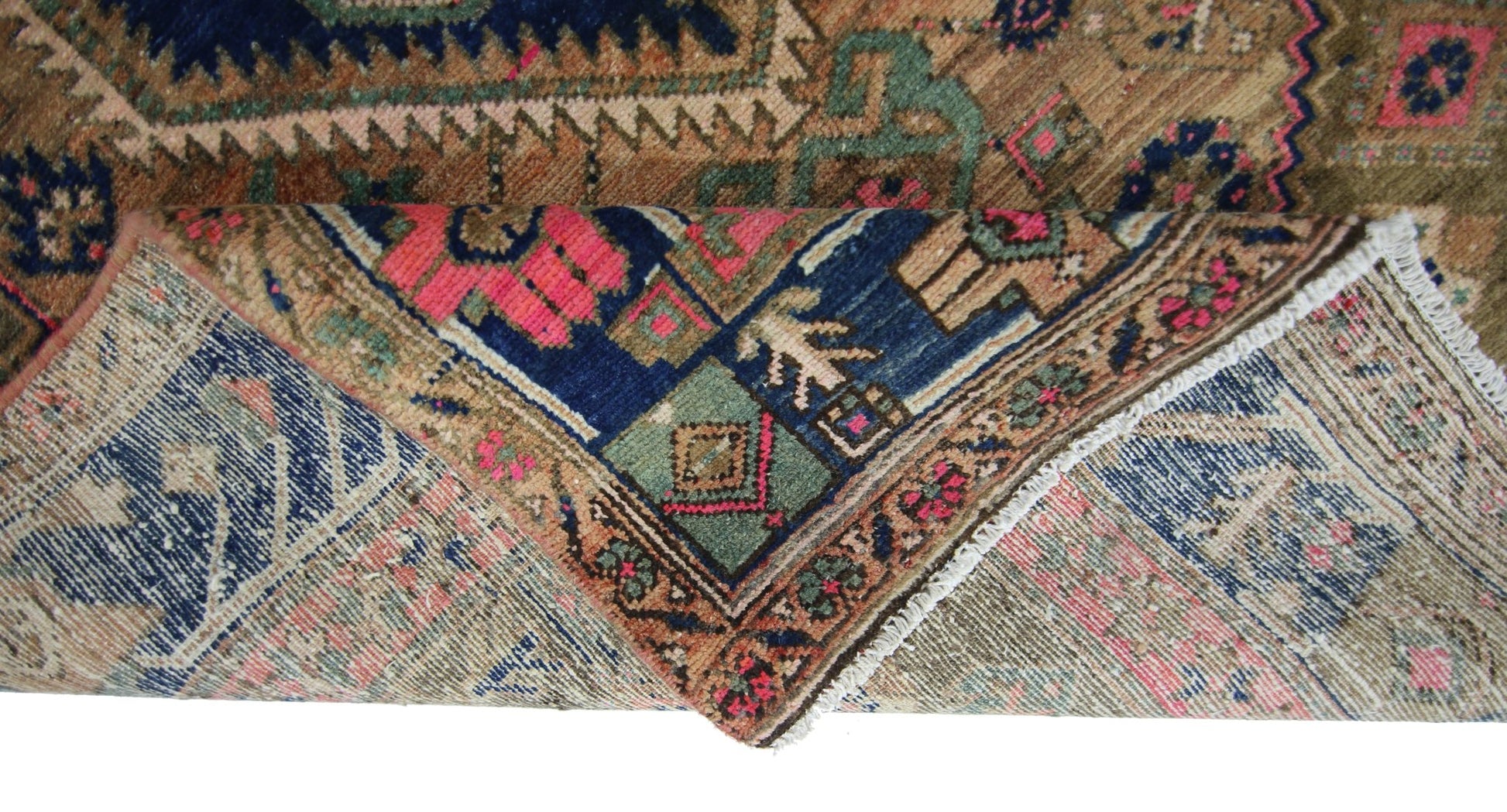 A vintage Persian Hamadan rug with a folded corner revealing its intricate geometric wool pattern.
