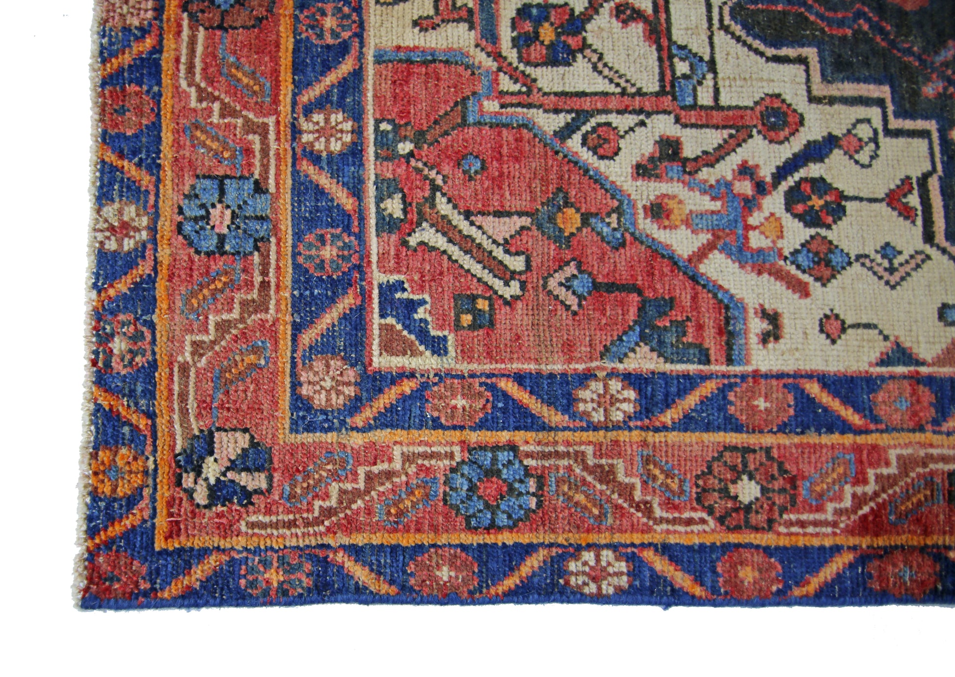 A corner view of a vintage Persian rug featuring intricate floral patterns in red, blue, and cream.