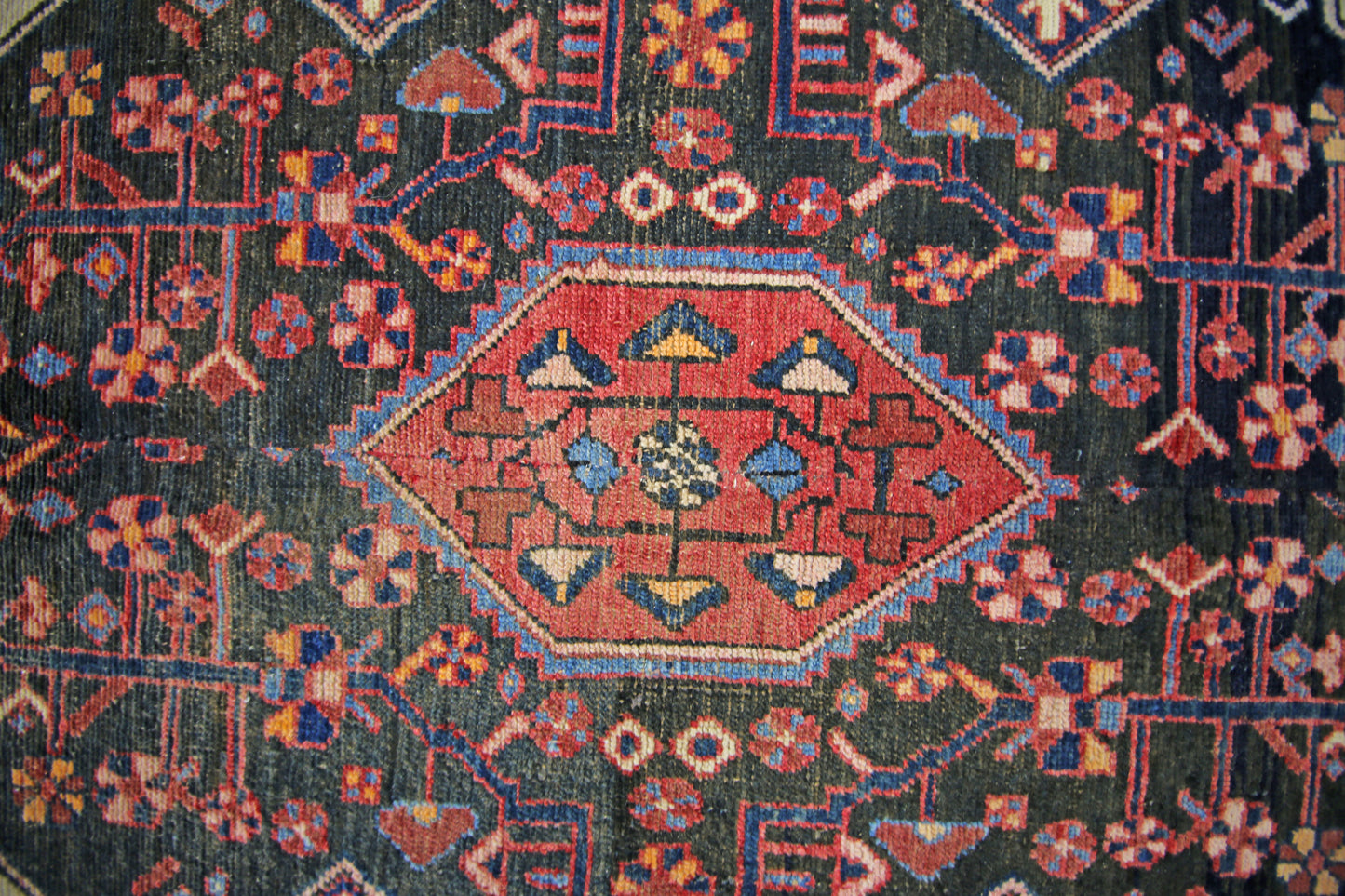 A vintage Persian rug featuring a central red diamond medallion with intricate geometric patterns.