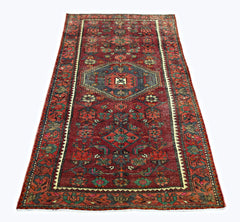 A rectangular vintage Persian rug featuring a red field with intricate geometric floral patterns.