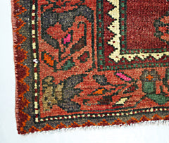 A close-up of a vintage Persian rug featuring intricate geometric patterns in red and dark tones.