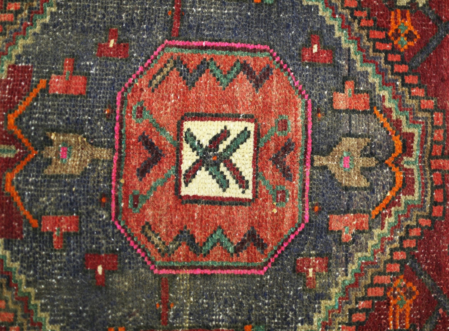 A vintage handmade Persian rug featuring a central geometric medallion in red and blue tones.