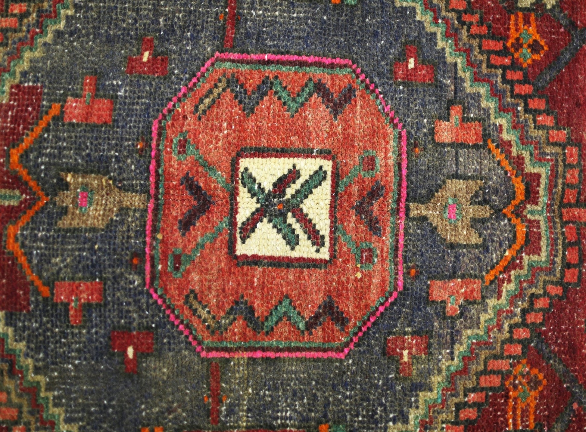 A vintage handmade Persian rug featuring a central geometric medallion in red and blue tones.