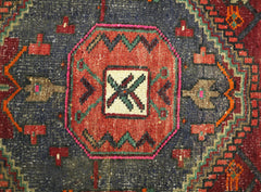 A vintage handmade Persian rug featuring a central geometric medallion in red and blue tones.