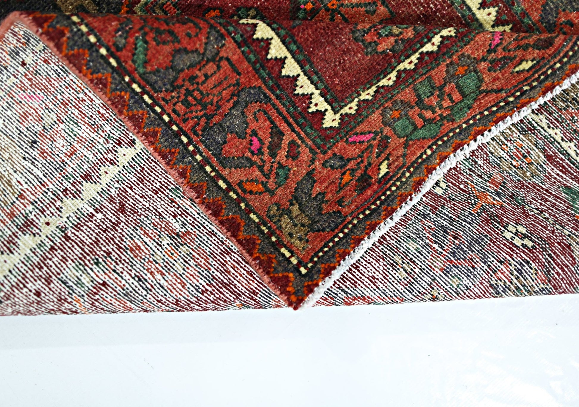 A folded vintage Persian rug featuring intricate geometric patterns in red, green, and cream.