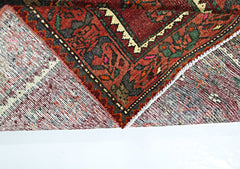 A folded vintage Persian rug featuring intricate geometric patterns in red, green, and cream.