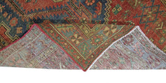 A vintage Persian Hamadan rug with a red and blue geometric pattern, shown folded to reveal its underside.