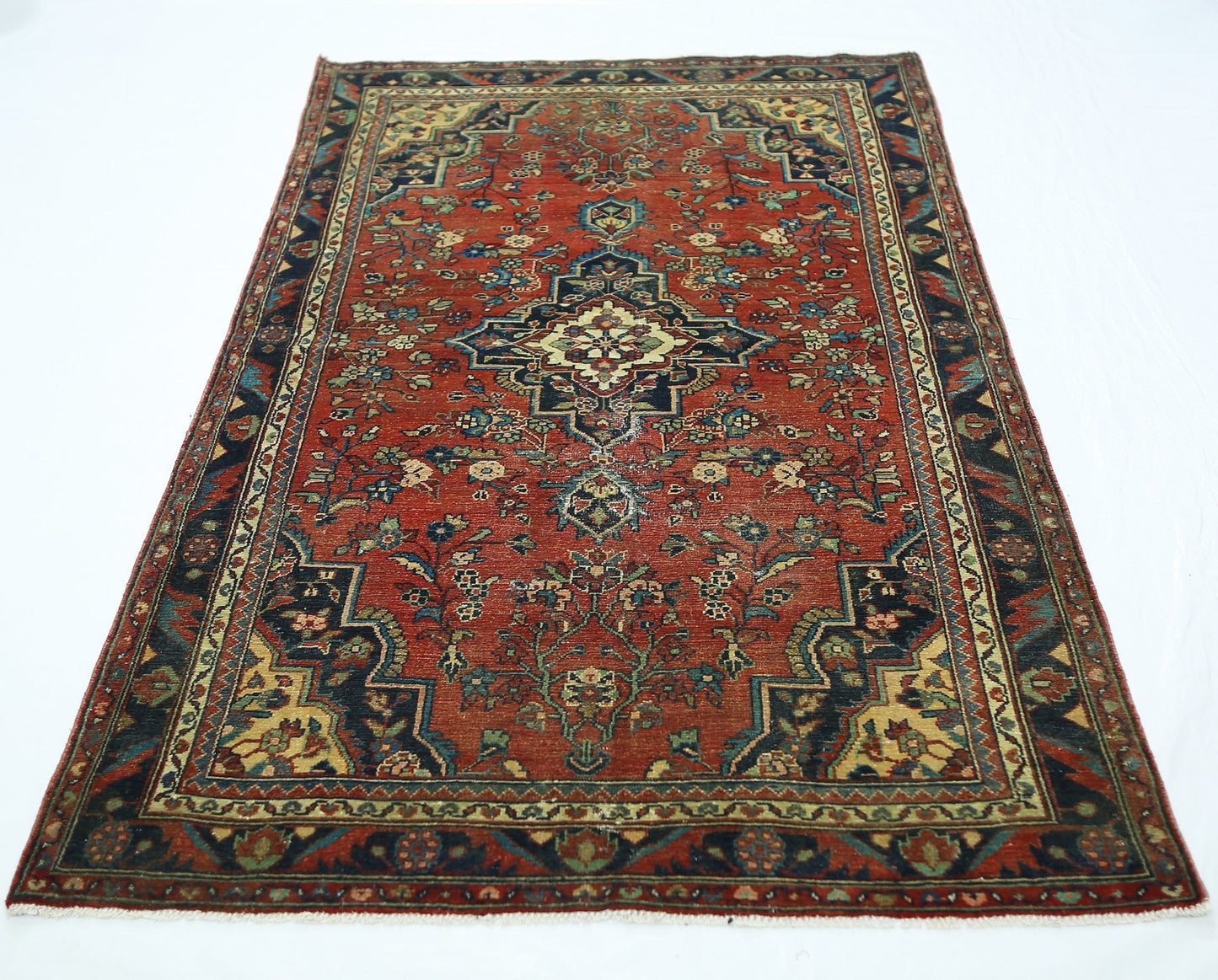 A vintage handmade Persian rug featuring a central medallion on a red field with floral patterns.