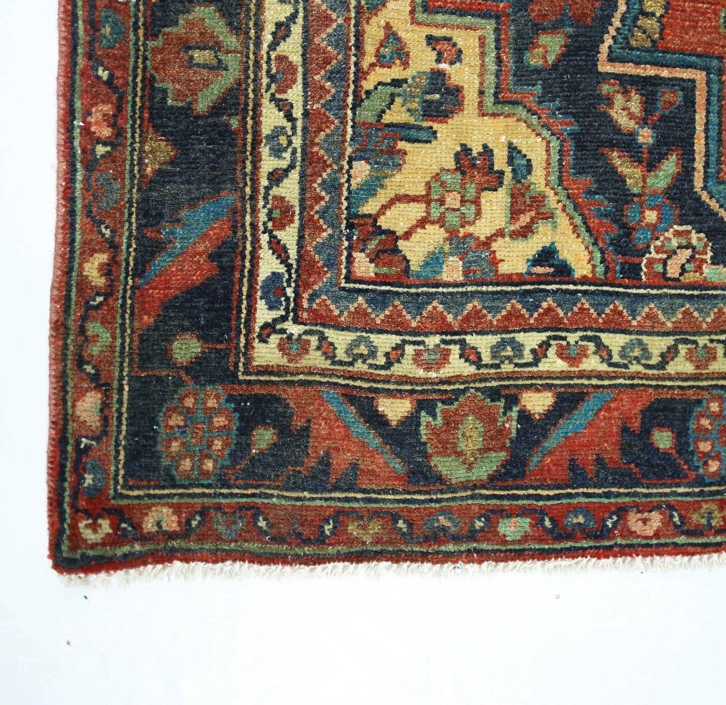 A corner view of a vintage Persian rug featuring intricate floral patterns in red, blue, and gold.