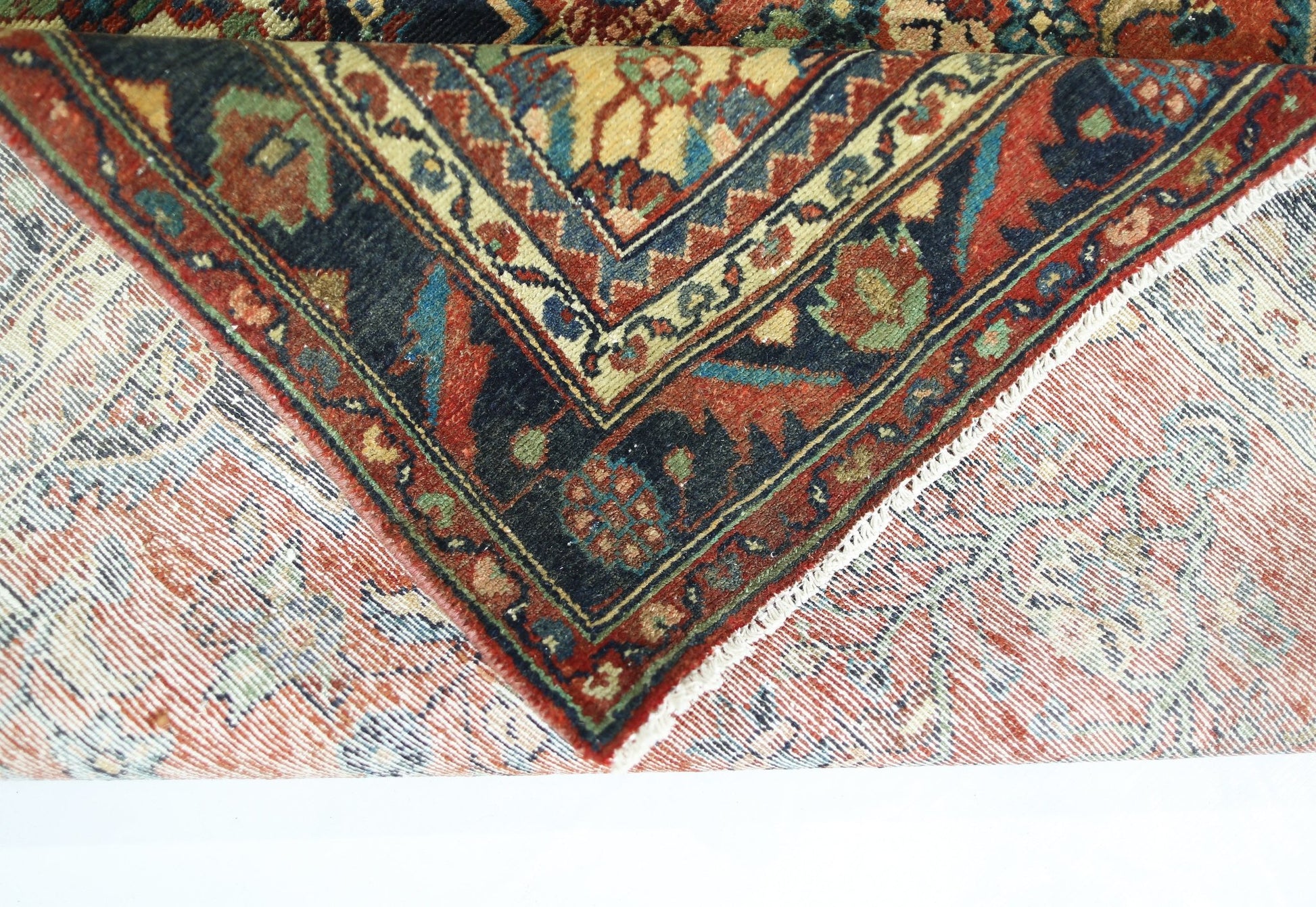 A corner of a vintage Persian rug is folded back to reveal its intricate floral pattern and weave.
