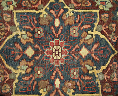 A vintage Persian rug featuring a detailed geometric floral medallion in blue, red, and tan tones.