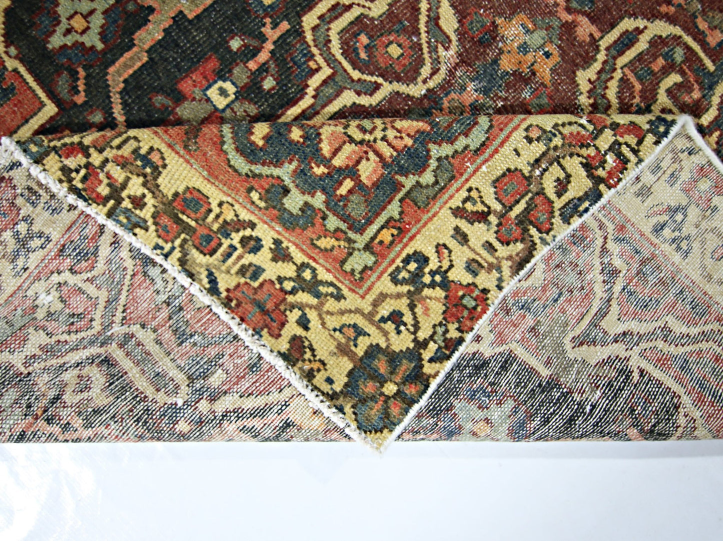 A corner of a vintage Persian rug is folded over to reveal its intricate wool pile and cotton base.