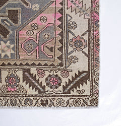 A vintage Persian Hamadan rug featuring geometric floral patterns in shades of pink, grey, and tan.