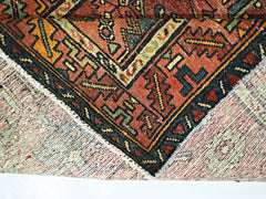 A vintage Persian Hamadan runner with a folded corner showing its wool pile and cotton foundation.