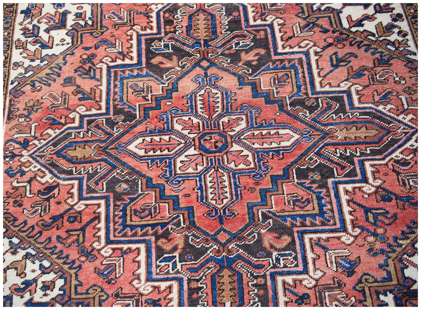 A vintage Persian Heriz rug featuring a geometric medallion pattern in red, blue, and cream tones.