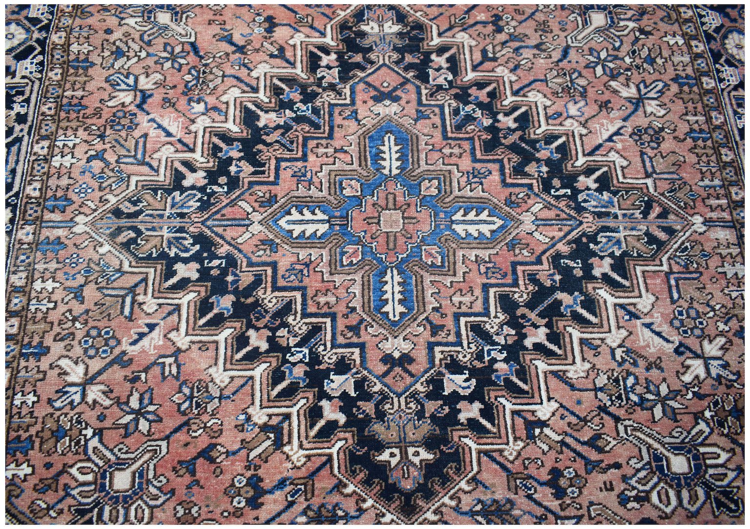 A vintage handwoven Persian Heriz rug featuring a geometric medallion in blue, pink, and cream.