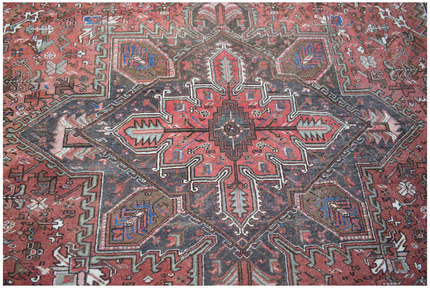 A vintage handwoven Persian Heriz rug featuring a geometric medallion in red, blue, and brown.