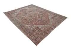 A vintage handwoven Persian Heriz rug featuring a geometric medallion on a faded red field.