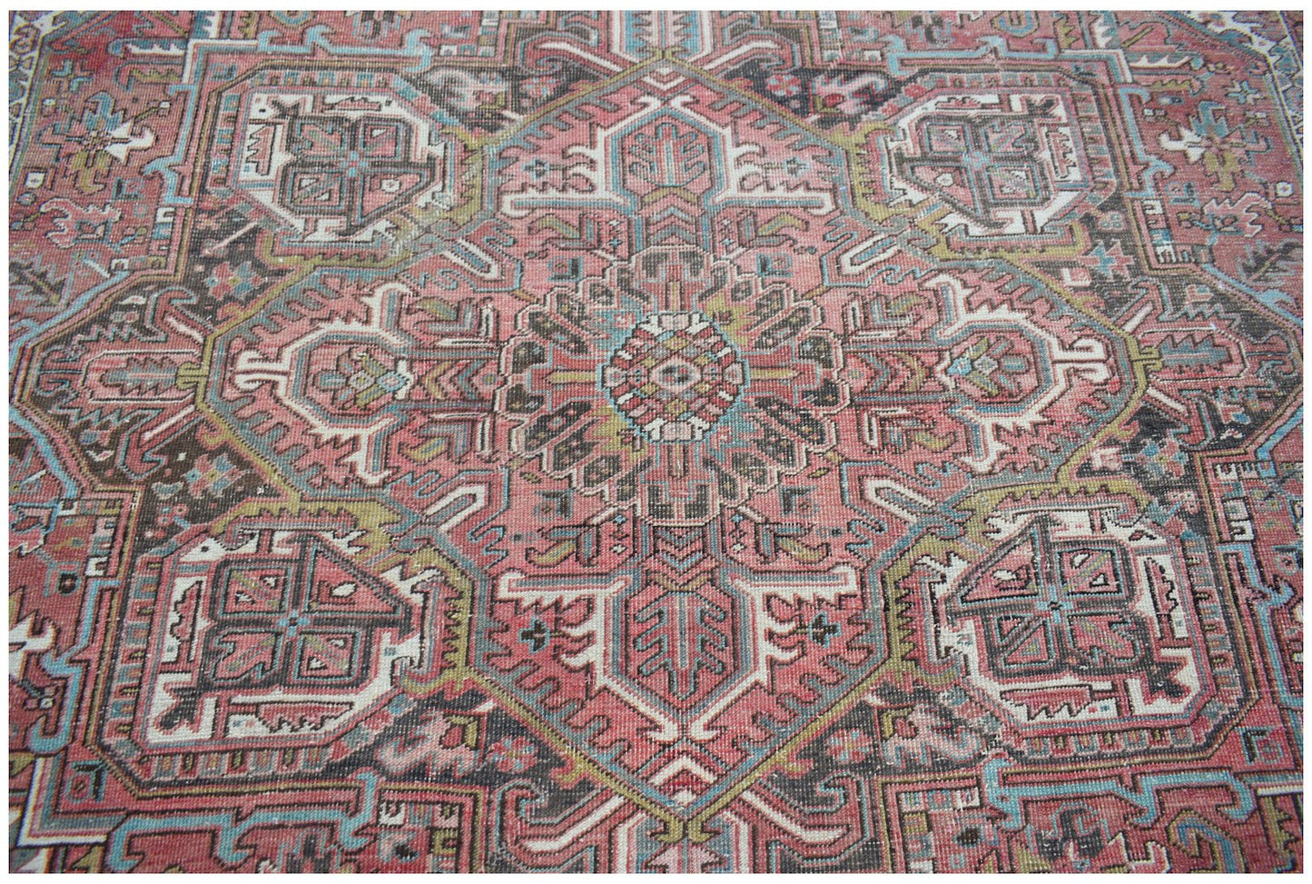 A vintage Persian Heriz rug featuring a geometric medallion pattern in pink, blue, and brown tones.