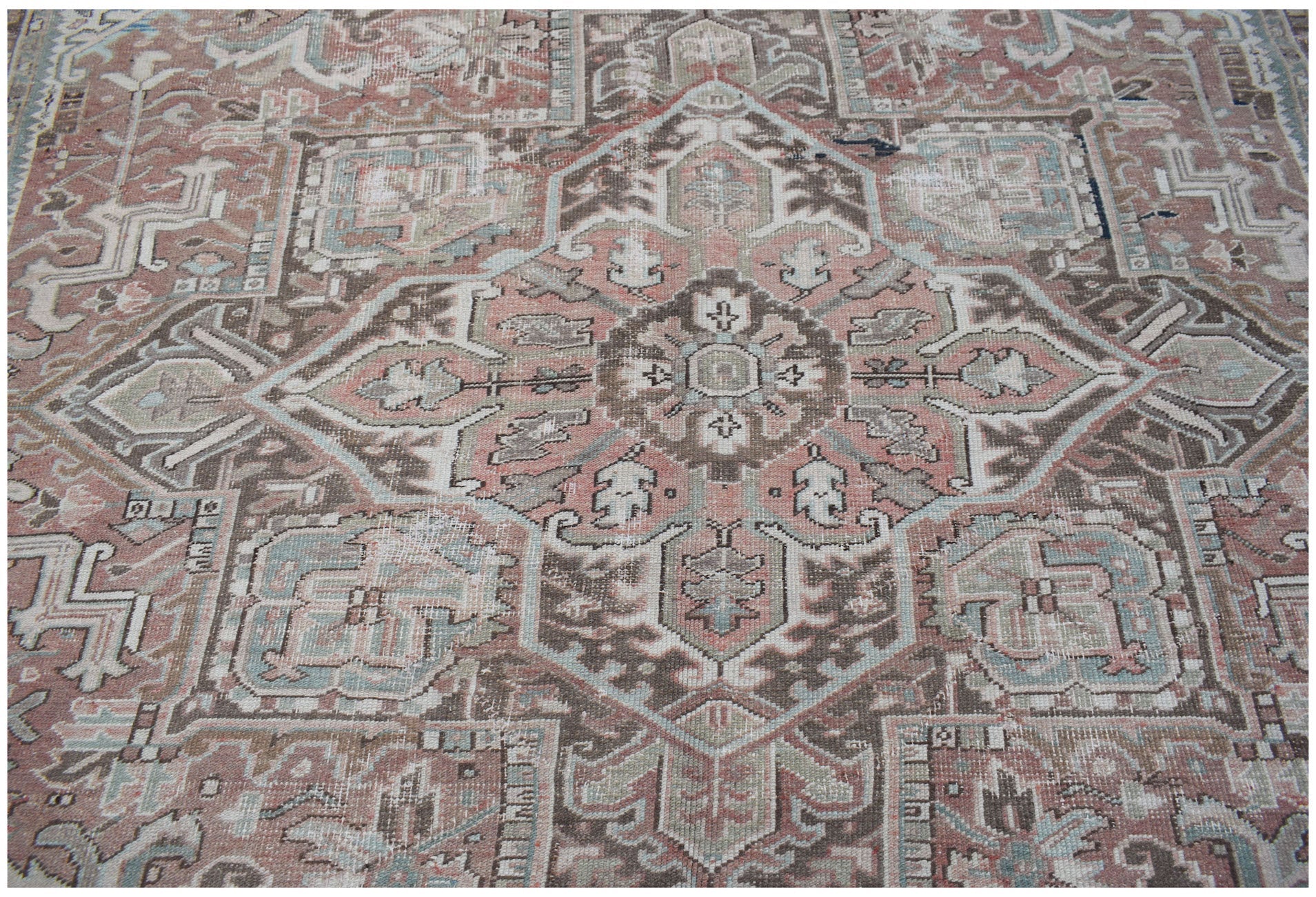 A vintage Persian Heriz rug featuring a geometric medallion pattern in muted pink, blue, and brown.
