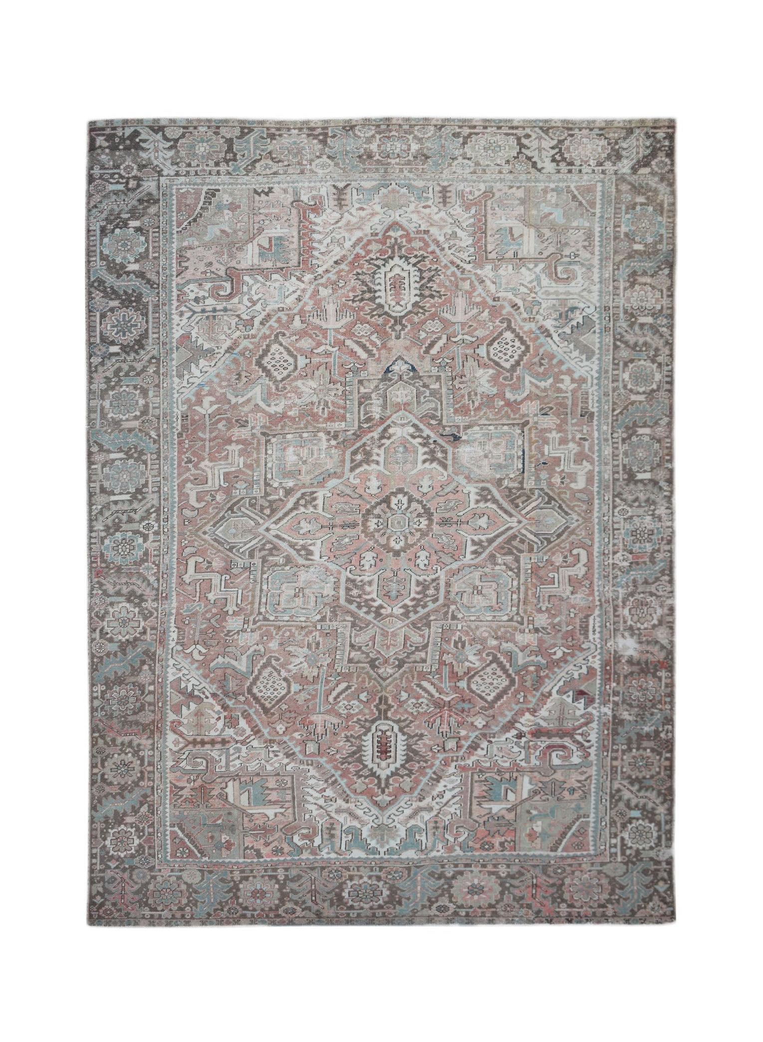 A vintage handwoven Persian Heriz rug featuring a geometric medallion in muted pink and brown tones.