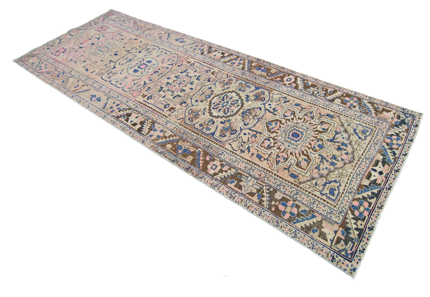 A vintage Persian Heriz runner rug featuring a geometric floral pattern in blue, pink, and tan.
