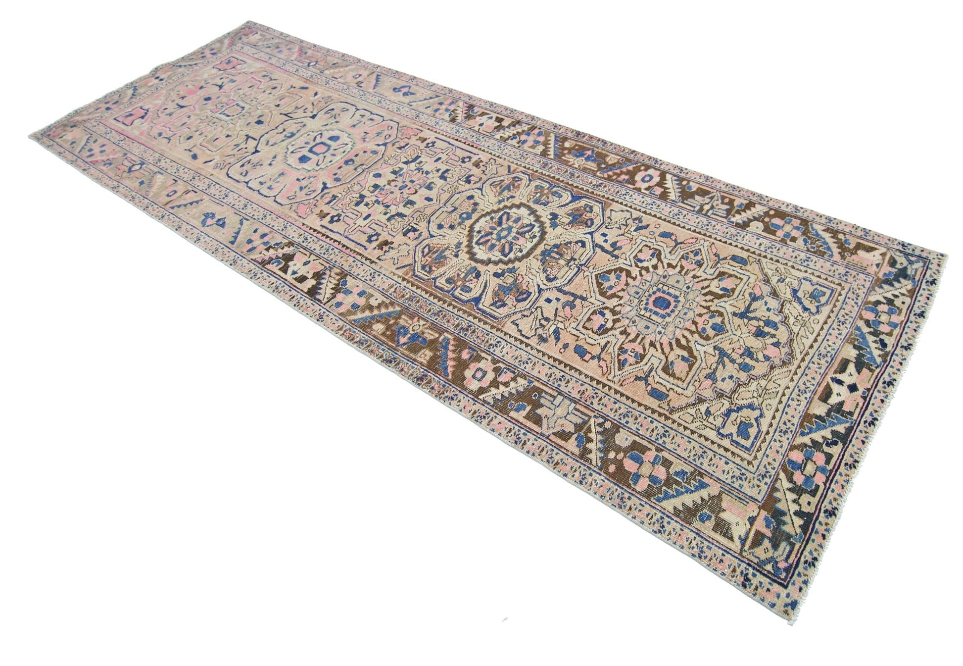 A vintage Persian Heriz runner rug featuring a geometric floral pattern in blue, pink, and tan.