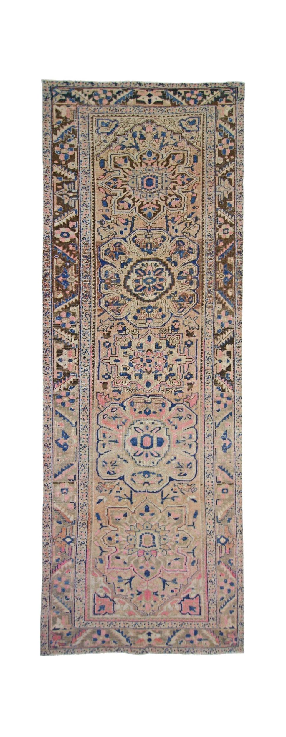 A vintage Persian Heriz runner rug featuring geometric floral medallions in pink, blue, and tan.