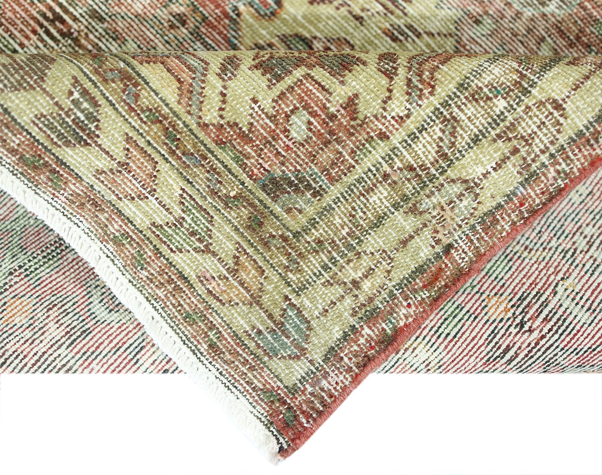 A folded vintage Persian rug featuring intricate floral patterns in muted red and green tones.