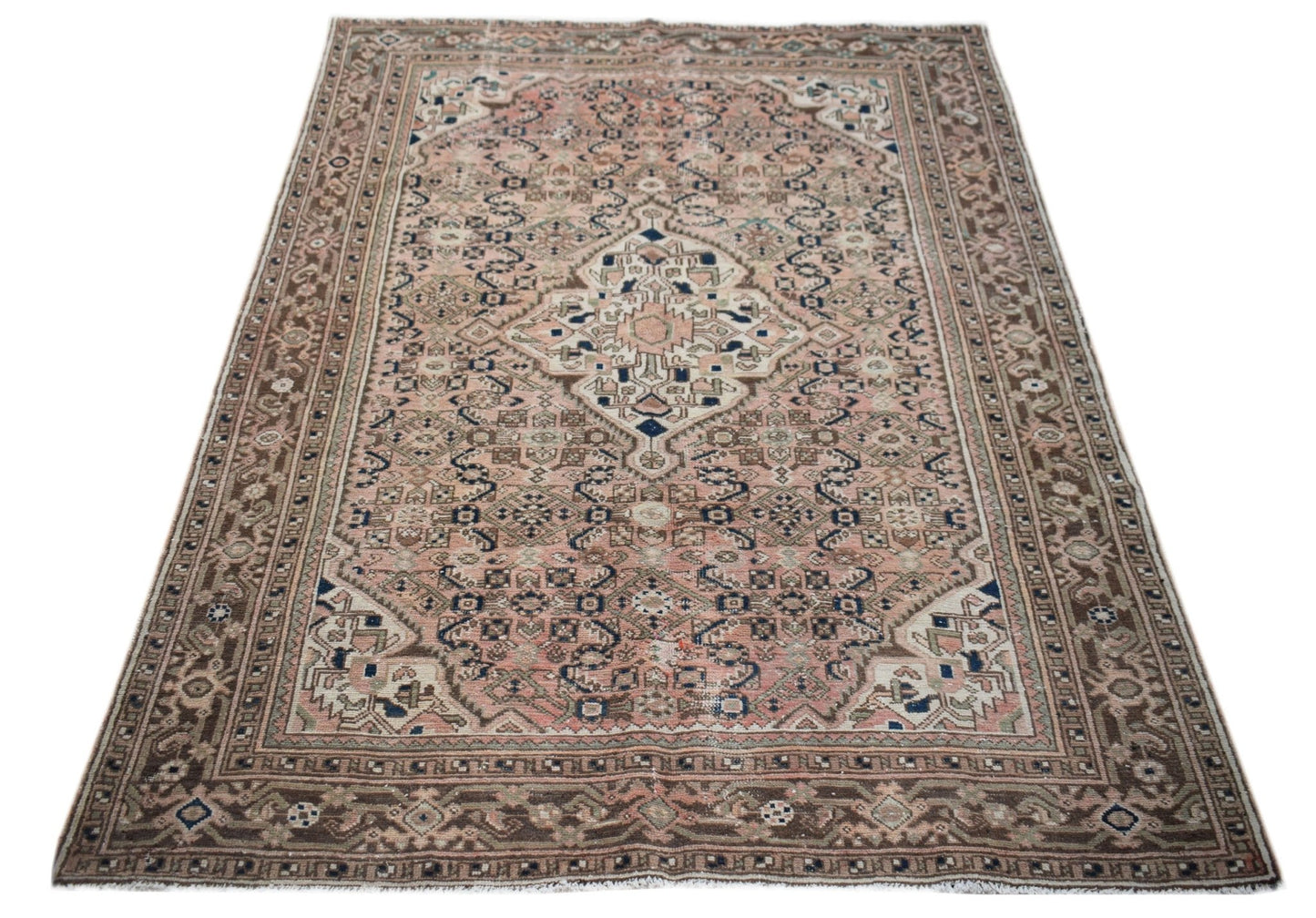 A vintage handwoven Persian rug featuring a central medallion on a faded pink and brown field.