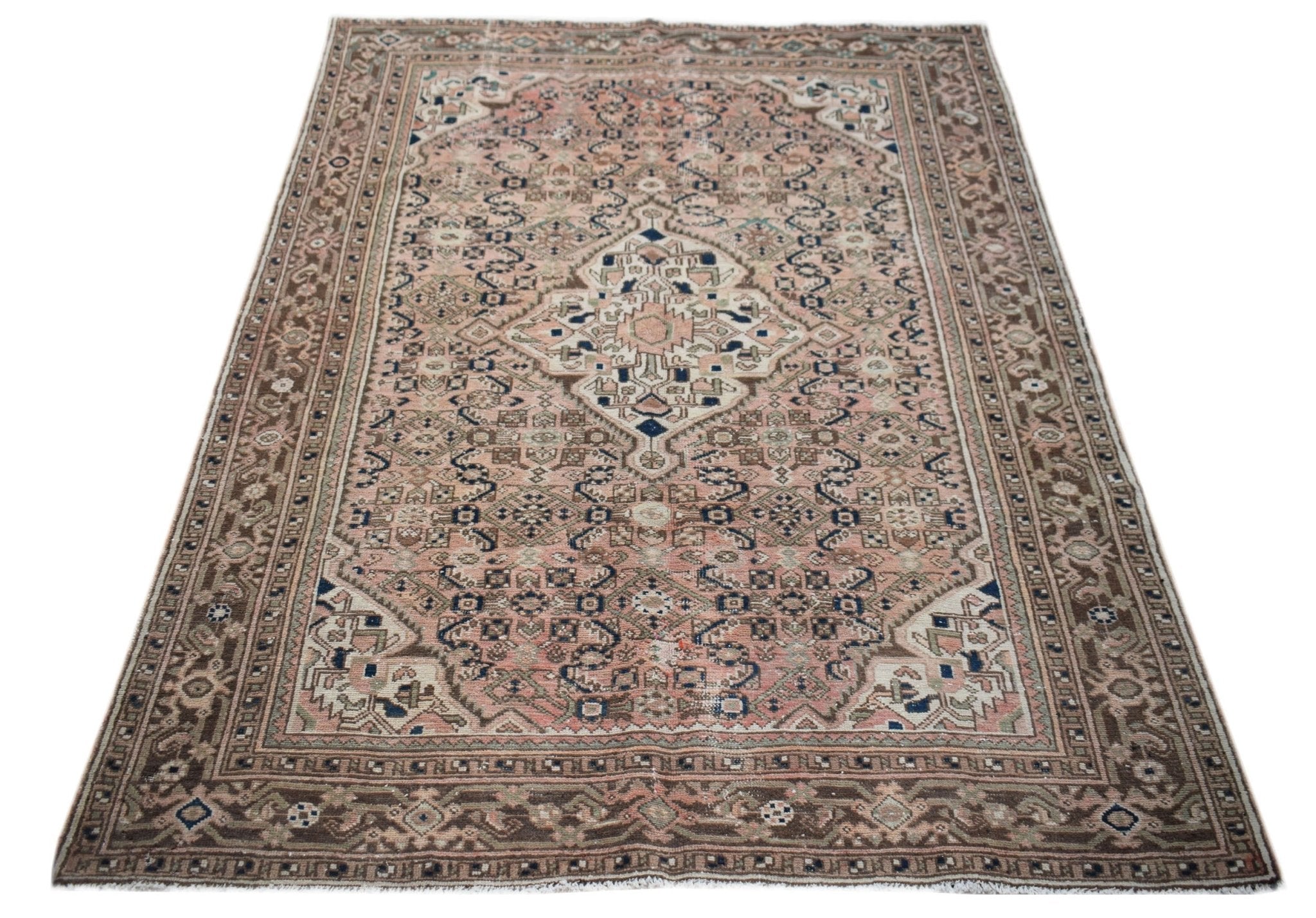 A vintage handwoven Persian rug featuring a central medallion on a faded pink and brown field.