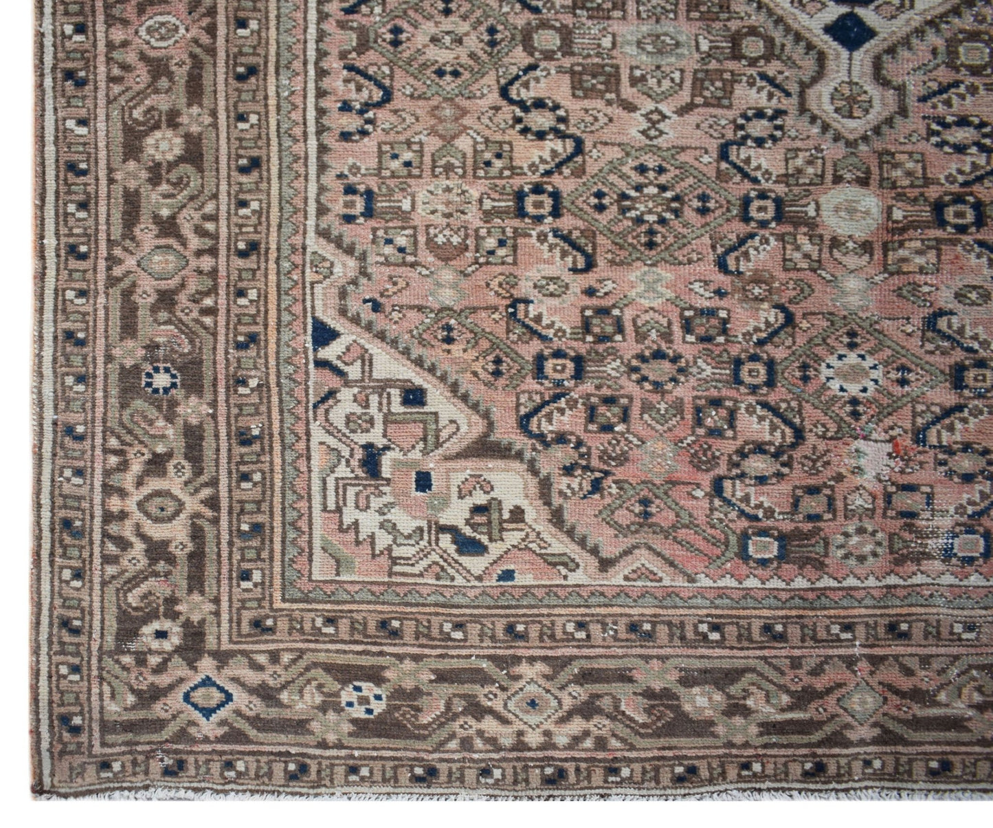 A vintage handwoven Persian rug featuring intricate geometric patterns in muted pink and brown.