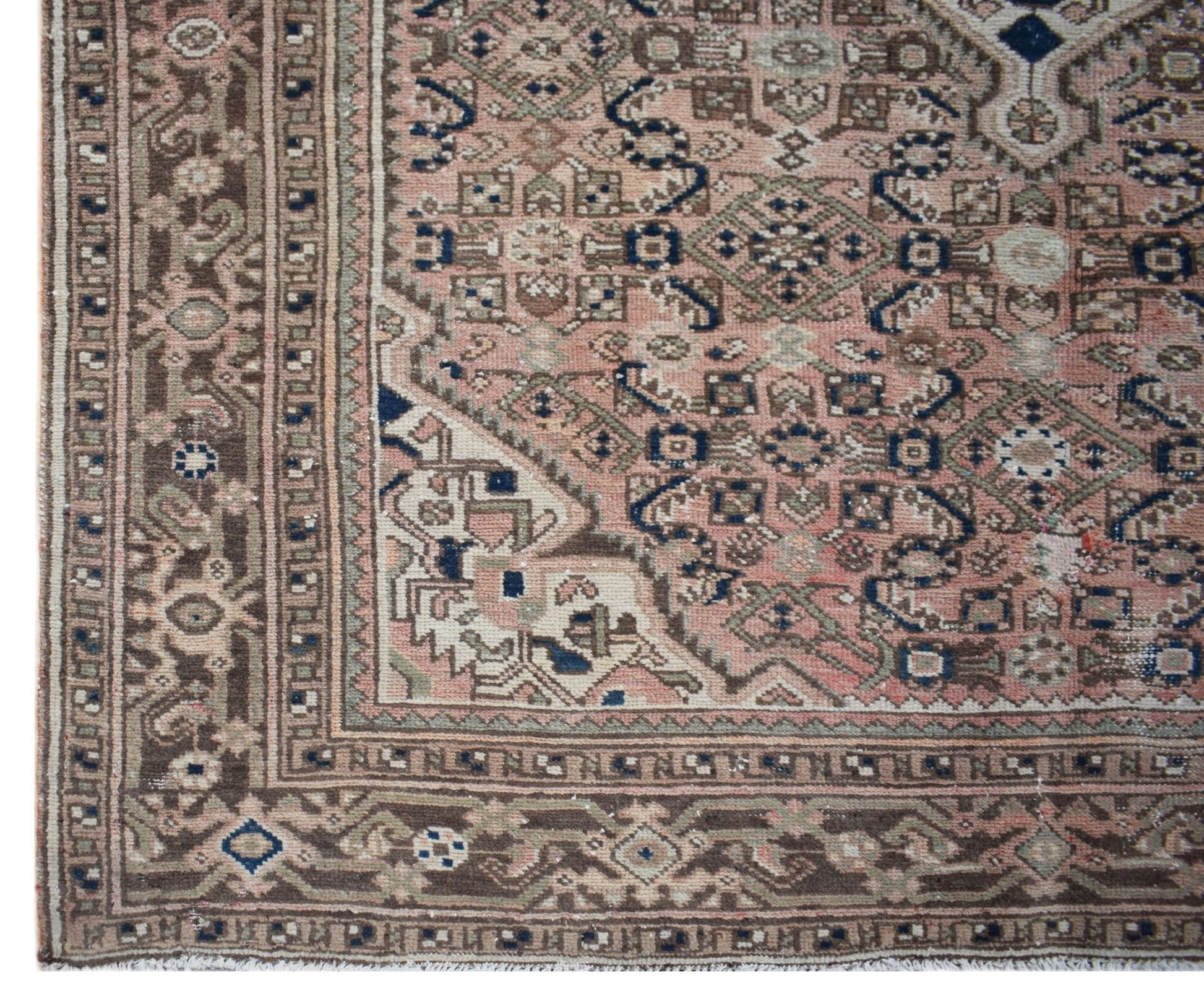 A vintage handwoven Persian rug featuring intricate geometric patterns in muted pink and brown.