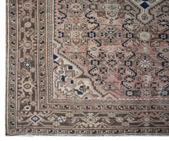 A vintage handwoven Persian rug featuring intricate geometric patterns in muted pink and brown.