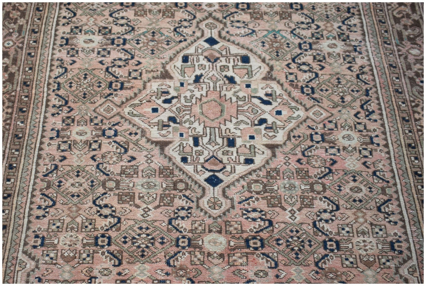 A vintage handwoven Persian rug featuring a central medallion in muted pink, blue, and brown tones.