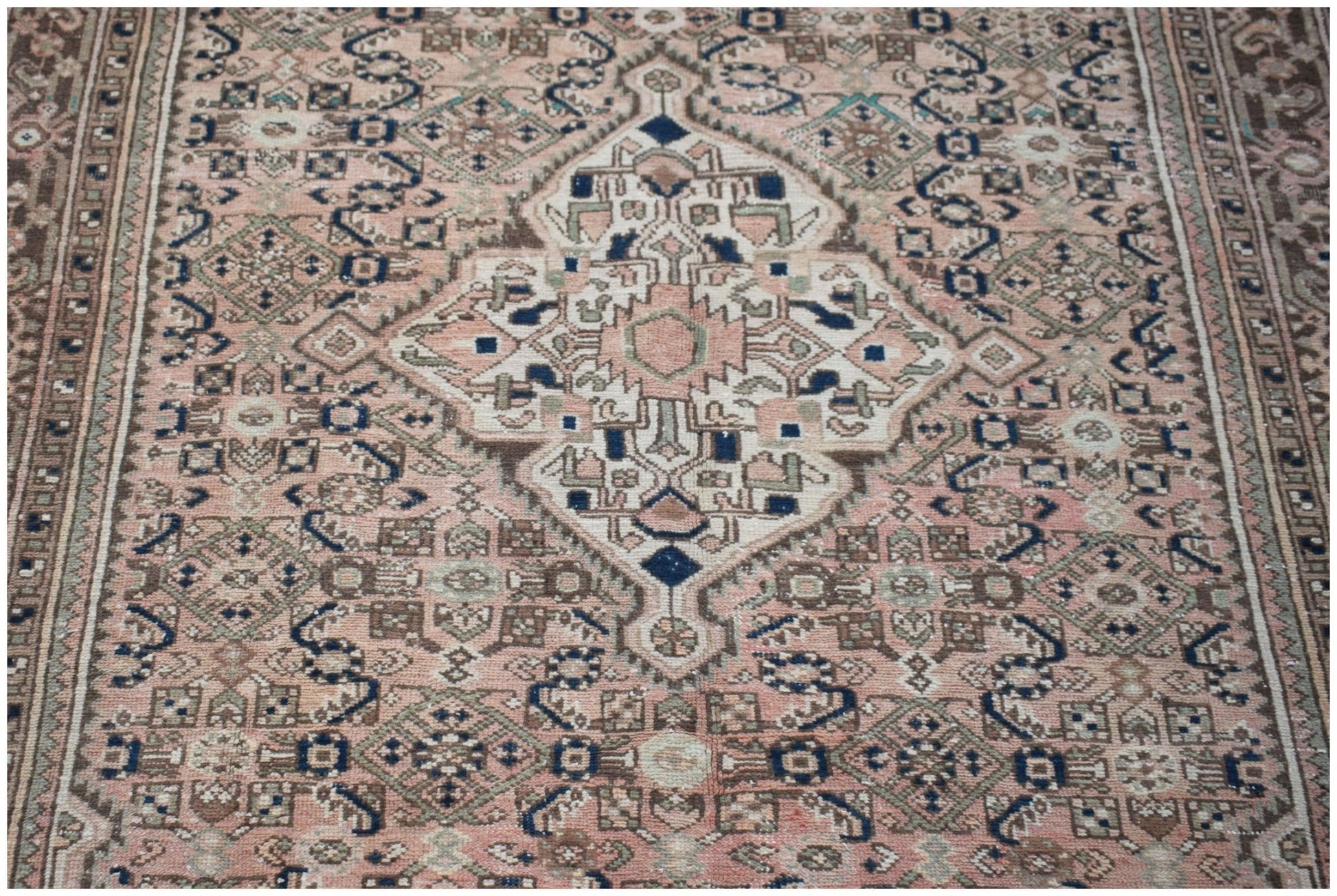 A vintage handwoven Persian rug featuring a central medallion in muted pink, blue, and brown tones.
